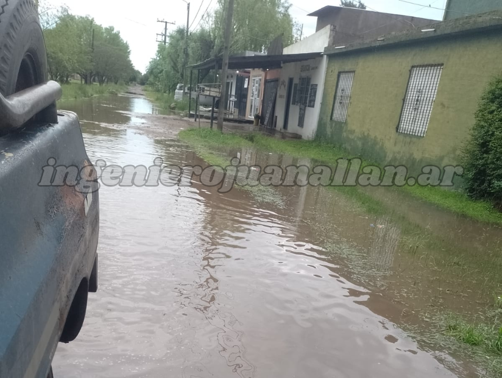 Calle de tierra convertida en un río marrón junto a una camioneta estacionada en Cinco Esquinas