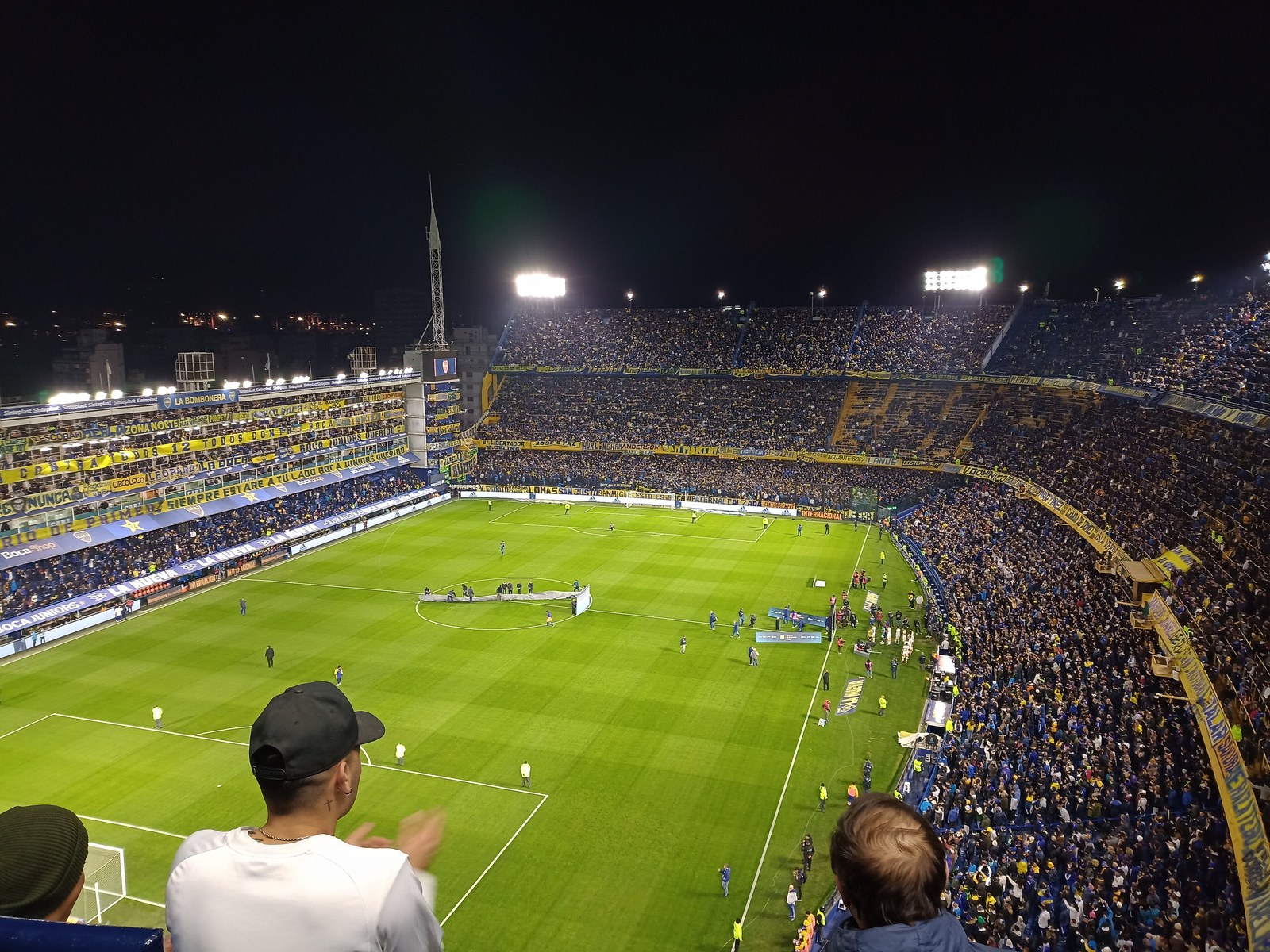 La Bombonera de noche, con las tribunas llenas de hinchas de Boca y los jugadores en el campo de juego iluminado antes de un partido