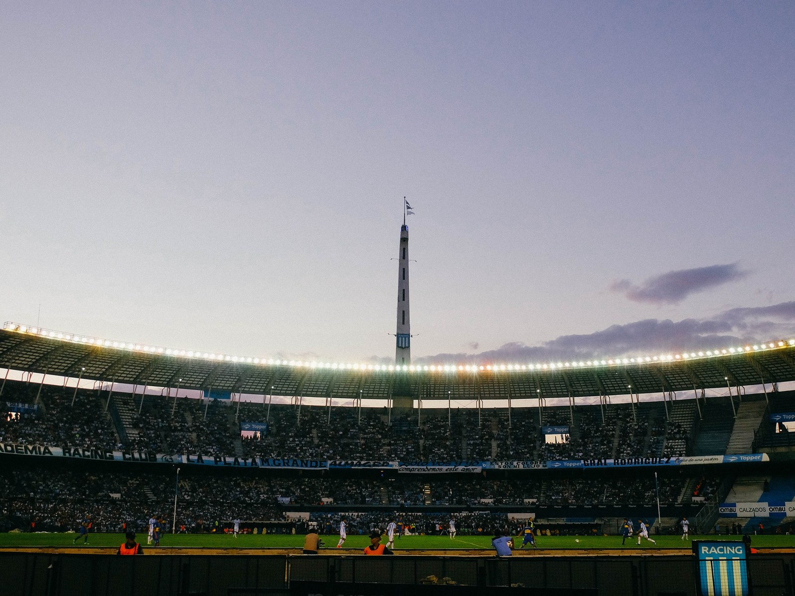El estadio Presidente Perón, el Cilindro de Avellaneda, al atardecer con las tribunas llenas, las luces del techo encendidas y un partido en juego