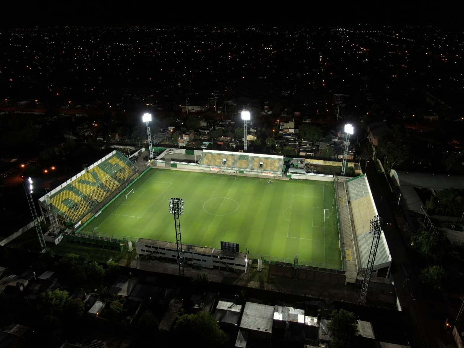 Vista aérea nocturna del estadio Norberto Tito Tomaghello de Defensa y Justicia, en Florencio Varela, con el campo iluminado y las tribunas verdes y amarillas
