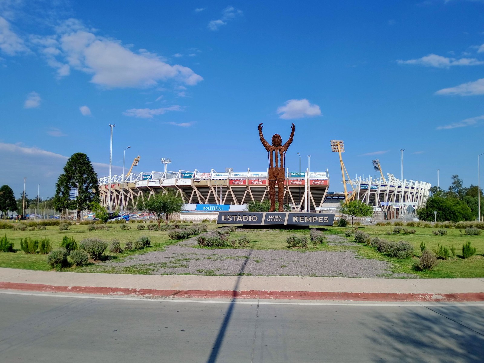 Ingreso al estadio Mario Alberto Kempes de Córdoba, con la escultura de un jugador con los brazos en alto, el cartel con el nombre del estadio y las tribunas al fondo bajo un cielo azul