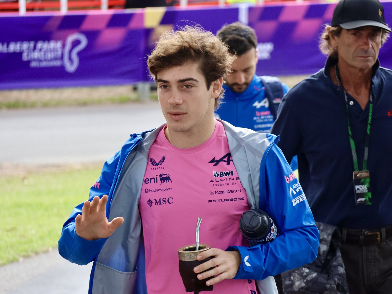 Franco Colapinto con campera azul y remera rosa de Alpine saluda con la mano mientras camina en un circuito