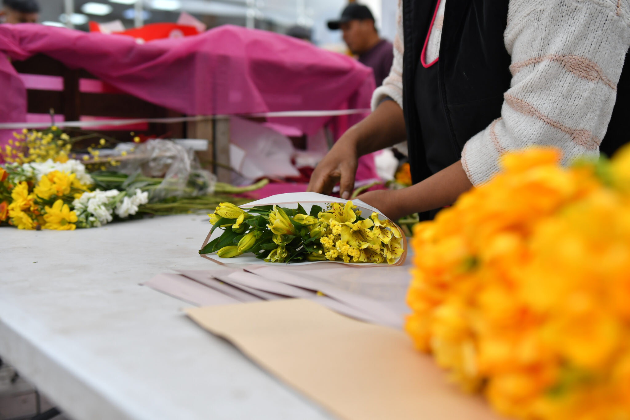 Manos de un floricultor envuelven un ramo de flores amarillas en papel kraft sobre una mesa de feria