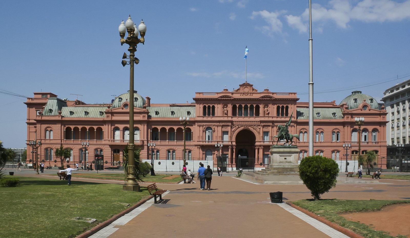 Fachada rosa de la Casa Rosada vista desde Plaza de Mayo, con la bandera argentina en el mástil central y el monumento a Belgrano a un costado