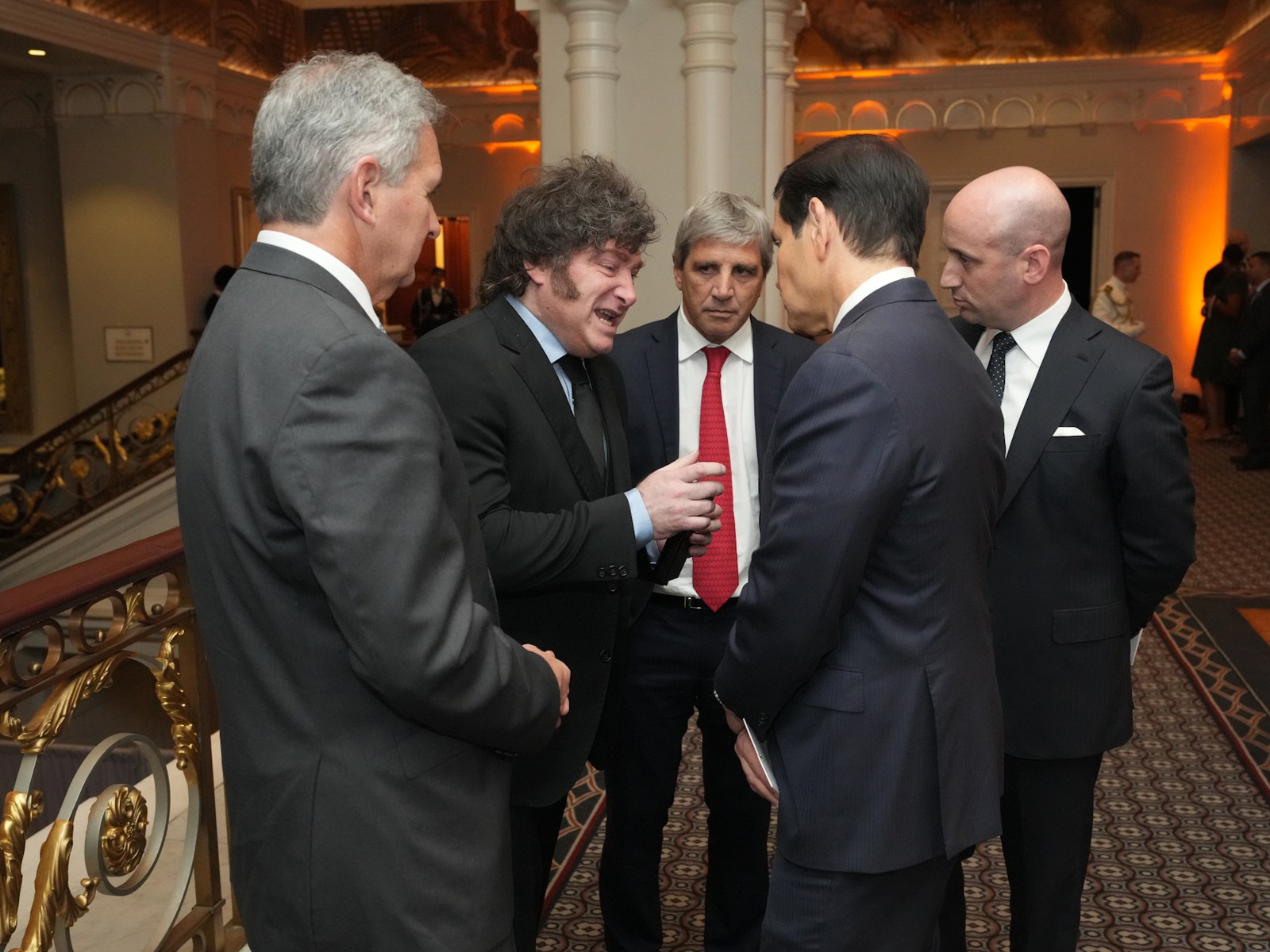 Javier Milei habla con Marco Rubio, que está de espaldas, en un salón de un hotel de Nueva York junto a otros funcionarios de traje