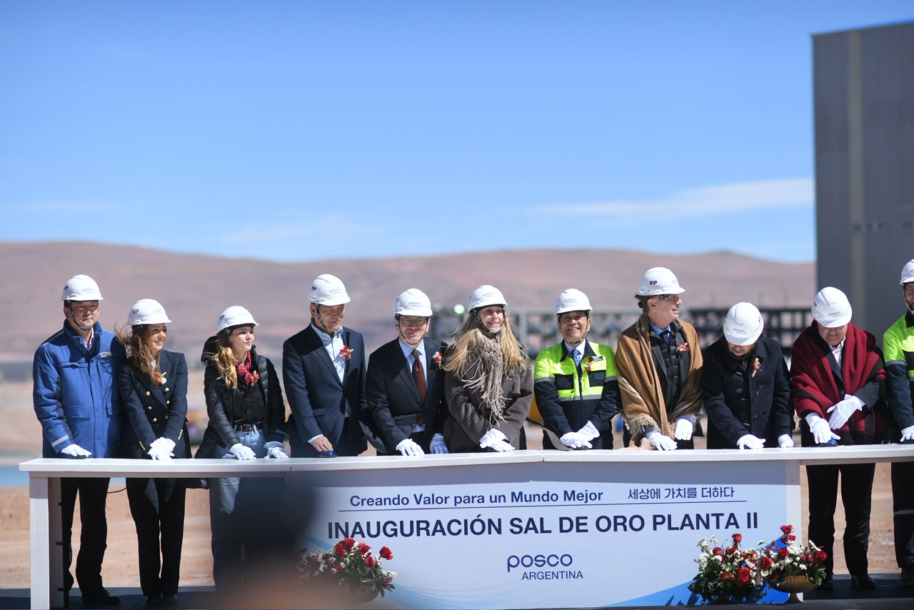 Funcionarios y directivos con cascos blancos detrás de un atril con el cartel Inauguración Sal de Oro Planta II, con los cerros de la Puna de fondo