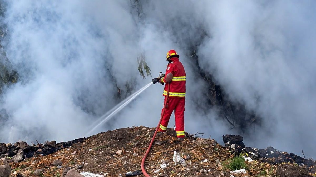Bombero con uniforme rojo apagando un incendio de monte entre el humo