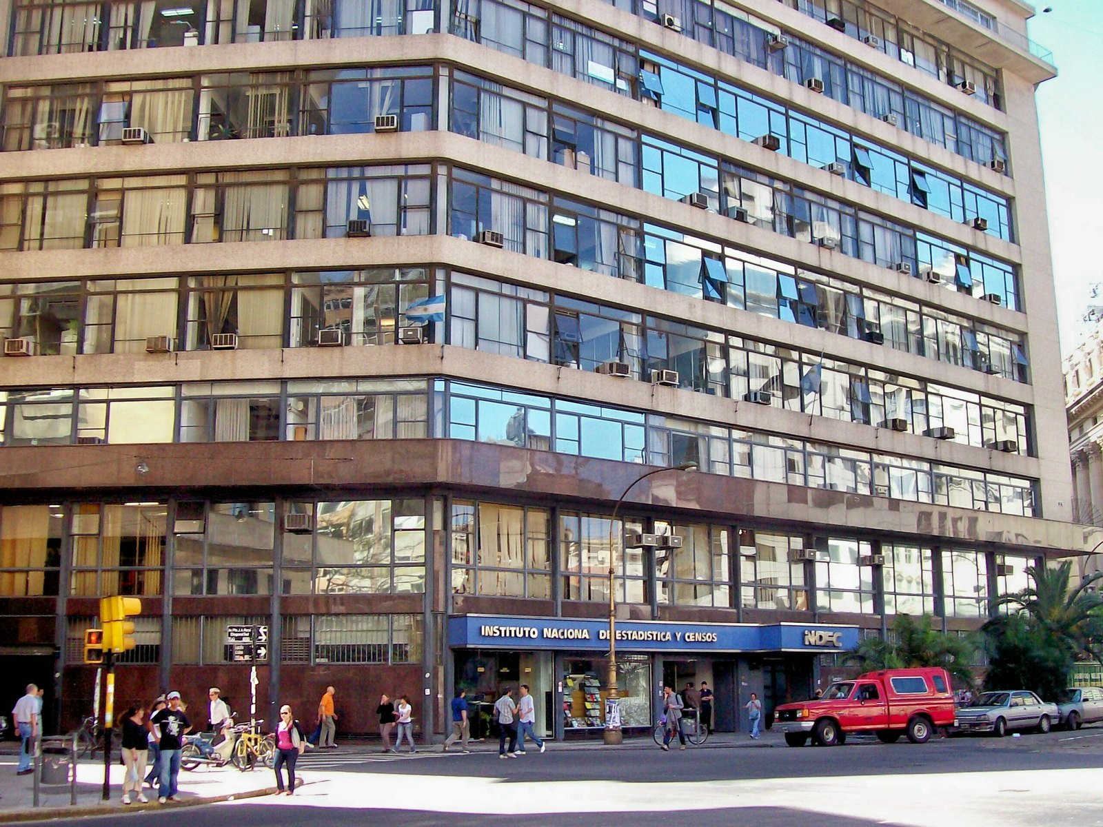 Edificio del Instituto Nacional de Estadística y Censos (INDEC) en Buenos Aires, una torre de oficinas con ventanales y el cartel azul del organismo en la planta baja, con gente caminando por la vereda