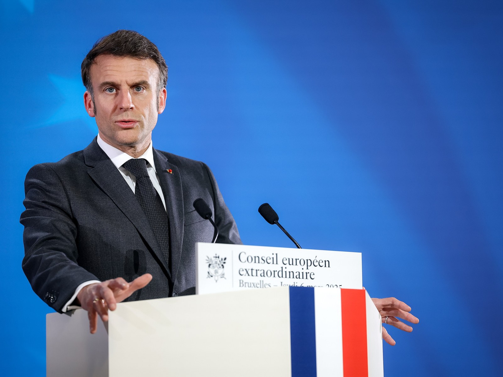Emmanuel Macron habla de pie detrás de un atril con la bandera de Francia, con traje oscuro y fondo azul