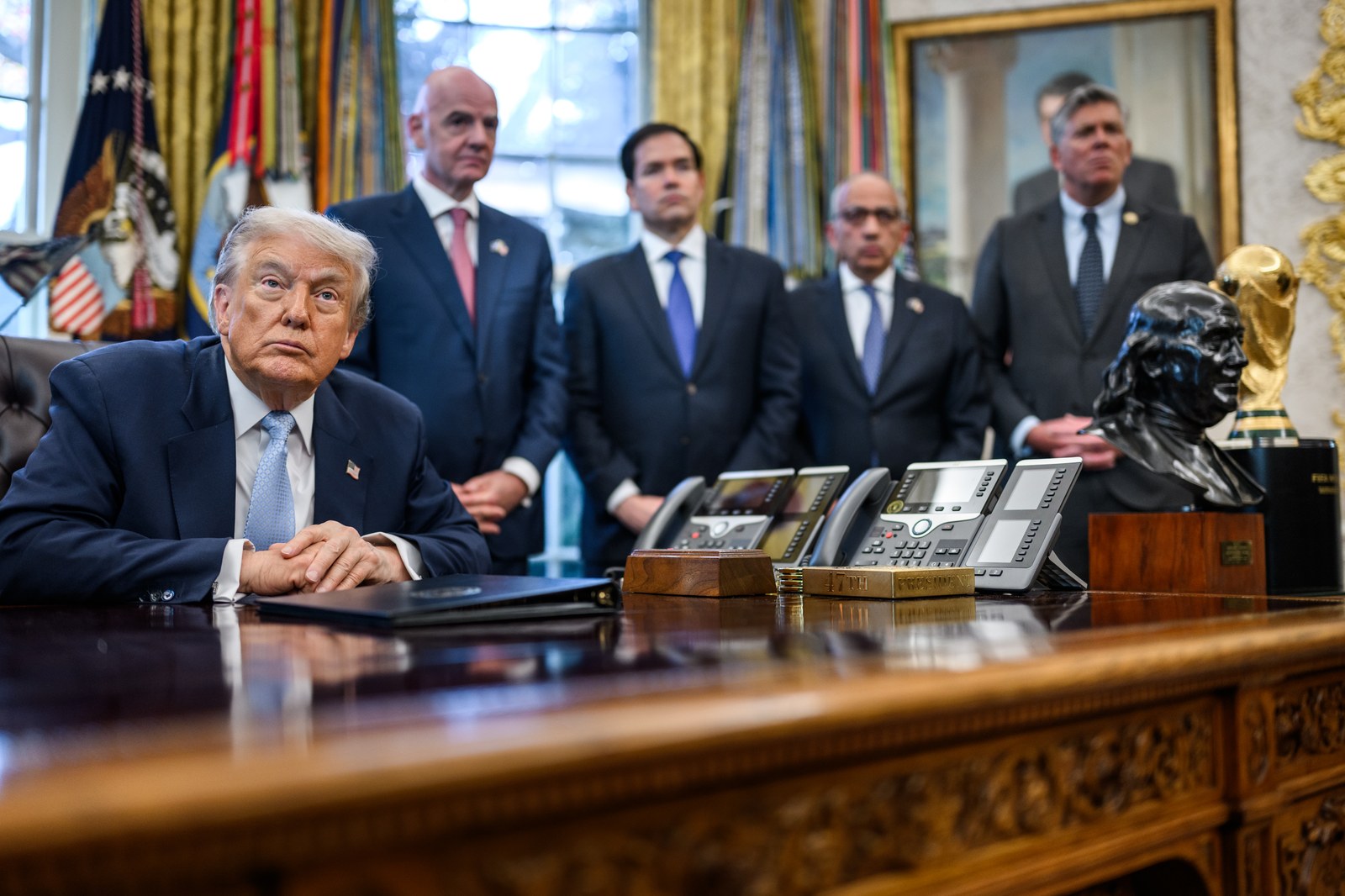 Donald Trump sentado en el Despacho Oval de la Casa Blanca, con traje oscuro y corbata celeste, frente a un escritorio con teléfonos y documentos