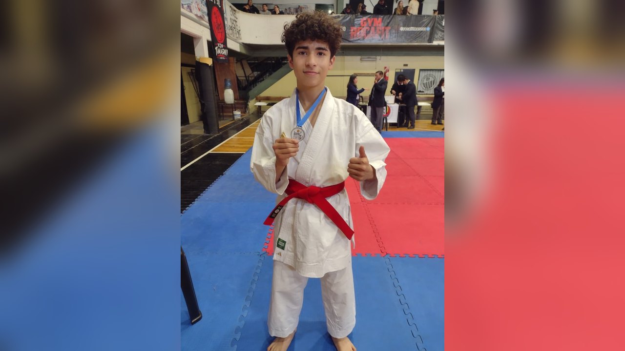 Joven karateca de Florencio Varela con karategi y cinturón rojo muestra su medalla del torneo regional
