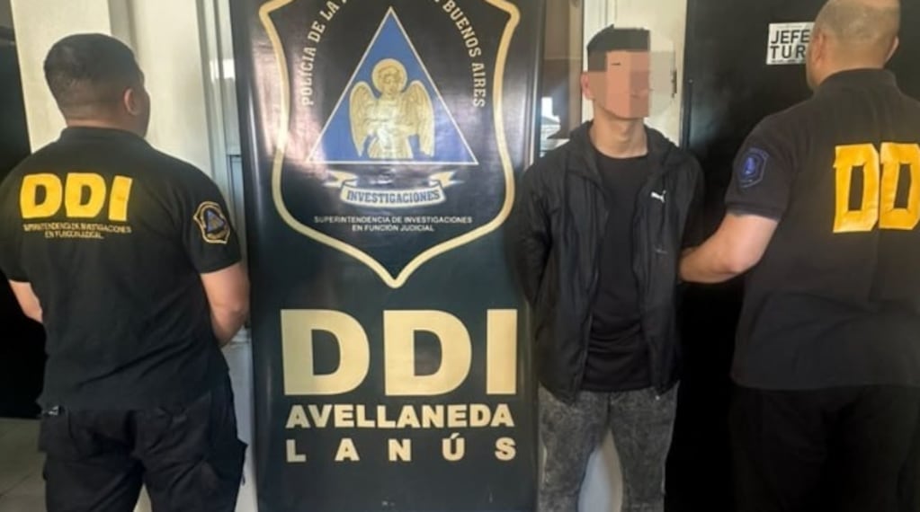 Un joven con el rostro difuminado, custodiado por dos efectivos de la DDI Avellaneda-Lanús frente a un cartel de la Policía bonaerense