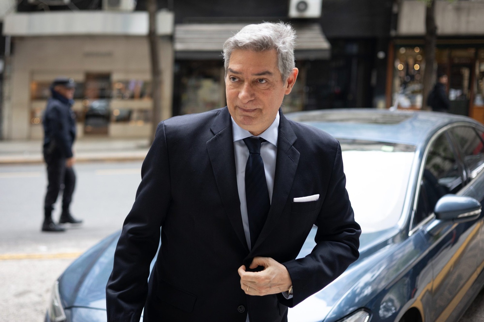 Horacio Rosatti, con traje oscuro y corbata, camina por una calle de la ciudad junto a un auto azul