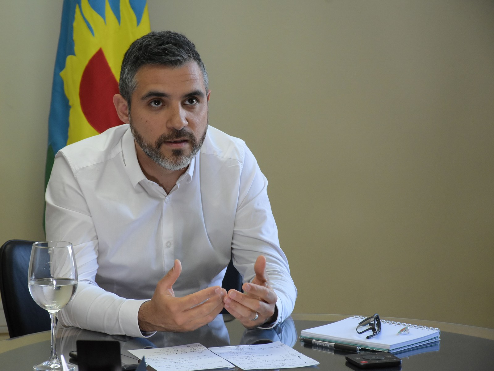 Cristian Girard, director ejecutivo de ARBA, con camisa blanca, sentado a una mesa con papeles, frente a la bandera de la provincia de Buenos Aires