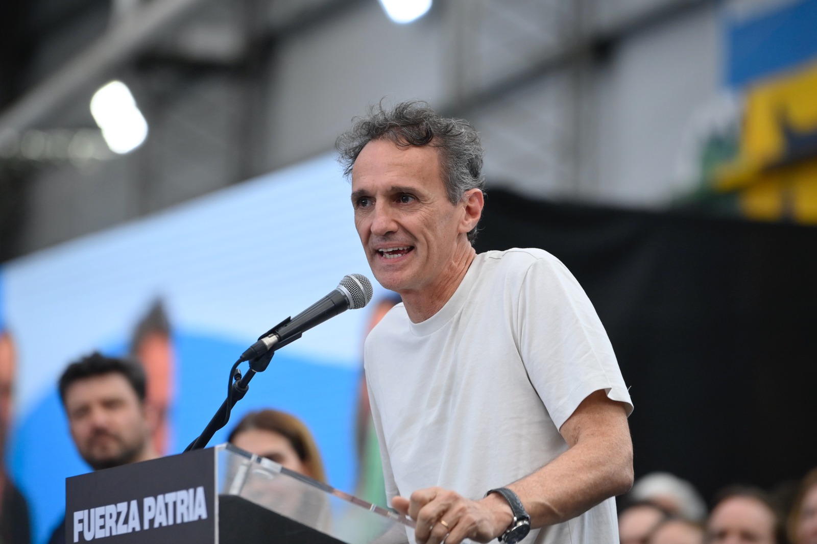 Gabriel Katopodis, con remera blanca, habla ante un micrófono en un atril con la leyenda Fuerza Patria